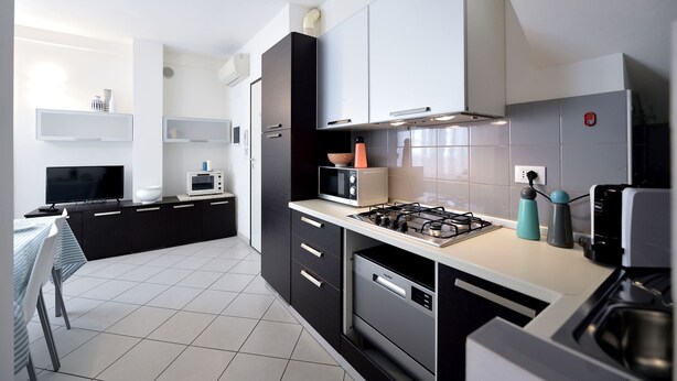 A modern kitchen with black and white cabinetry, a gas stove, a microwave, and a dishwasher. - Mina Suite - Double Apartment (Cattolica)