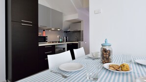 A modern kitchen with dark cabinets, a striped tablecloth, and a breakfast setting with cookies and a glass of water. - Mina Suite - Double Apartment (Cattolica)