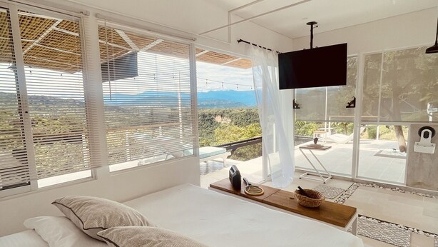 A modern bedroom with a large bed, a TV, and a view of the outdoors. - CasaDorothea (Apulo)