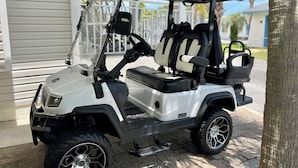 En vit golfbil parkerad utanför ett hus med en möblerad uteplats och en trappsteg för enkel tillgång.