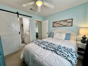 Une chambre à coucher comprenant un lit, un ventilateur de plafond, une table de chevet avec une lampe et un tableau représentant des poissons accroché au mur.