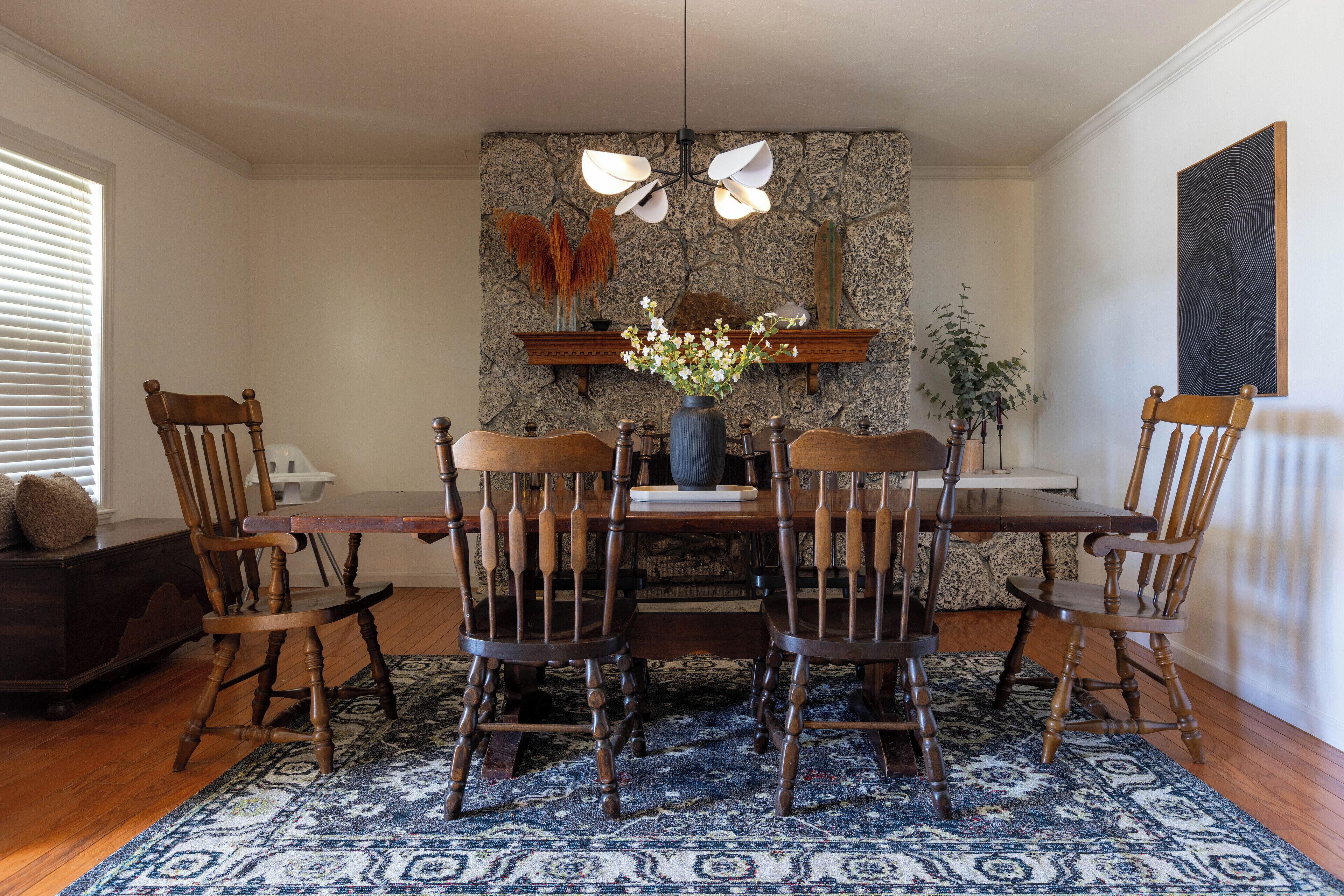 Un coin repas avec un mur en pierre, des chaises en bois, une table et un lustre.