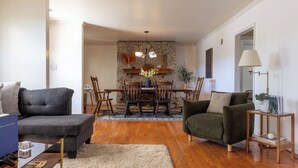 Een woonkamer met een grijze bank, een groene fauteuil, een houten eettafel met stoelen en een accentmuur van steen.