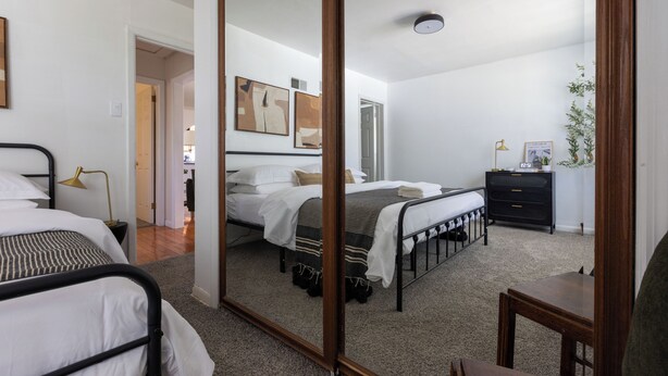 Een slaapkamer met twee bedden, een grote spiegel, een nachtkastje met een lamp, een dressoir en een plant.
