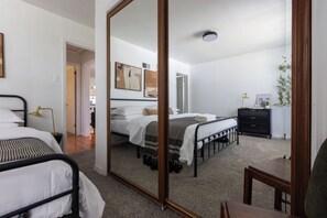A bedroom with two beds, a large mirror, a bedside table with a lamp, a dresser, and a plant. - Mid-Century Modern Estate in the heart of South County (St. Louis)