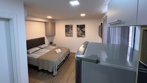 Een kleine slaapkamer met een bed, nachtkastje en een klein keukenhoekje.