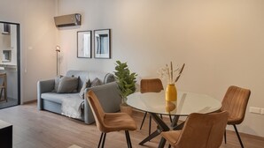 Una sala de estar moderna con una mesa de comedor de vidrio, sillas marrones, un sofá gris y una planta en maceta.