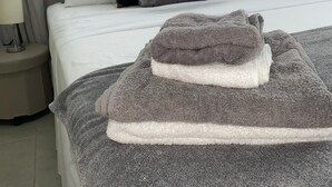 A neatly made bed with a grey blanket and a folded towel, a bedside lamp, and a window with blinds. - 73 Fairway Gardens Cozy 2-bedroom apartment in lovely Rendezvous with AC, WiFi (Rendezvous)
