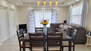 A dining area with a round table and chairs, a vase with flowers, a sofa with cushions, and a TV on a stand. - 73 Fairway Gardens Cozy 2-bedroom apartment in lovely Rendezvous with AC, WiFi (Rendezvous)