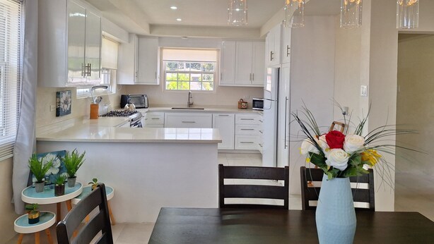 A modern kitchen with white cabinets, a central island, a dining area with a table and chairs, and pendant lighting. - 73 Fairway Gardens Cozy 2-bedroom apartment in lovely Rendezvous with AC, WiFi (Rendezvous)