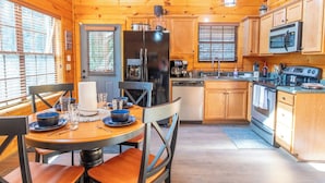 A wooden cabin interior with a dining area, kitchen, and a large refrigerator. - *Creekside 1BD + Loft Cabin! Hot Tub + Fire Pit!* (Sevierville)