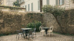 An outdoor patio area with a table and chairs, a stone wall, and a building in the background. - Rafael Green Home (Como)
