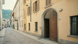 A narrow cobblestone street lined with yellow buildings, a wooden door, and a number '43' sign. - Rafael Green Home (Como)