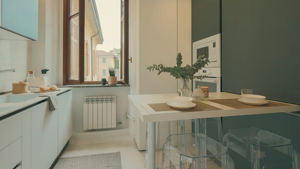 A modern kitchen with a large window, white cabinets, and a central island with stools. - Rafael Green Home (Como)