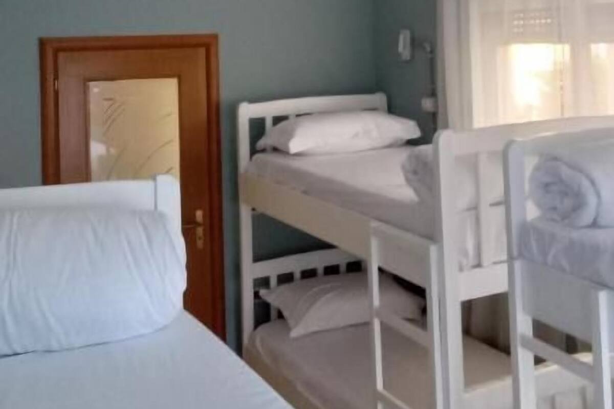 A room with bunk beds, a single bed, a door, and a window with curtains.