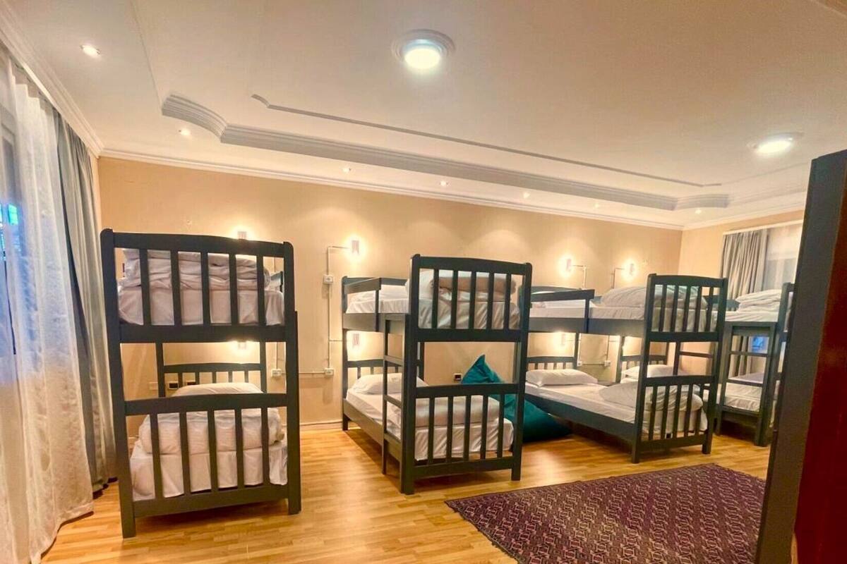 A room with bunk beds, wooden flooring, and a patterned rug.
