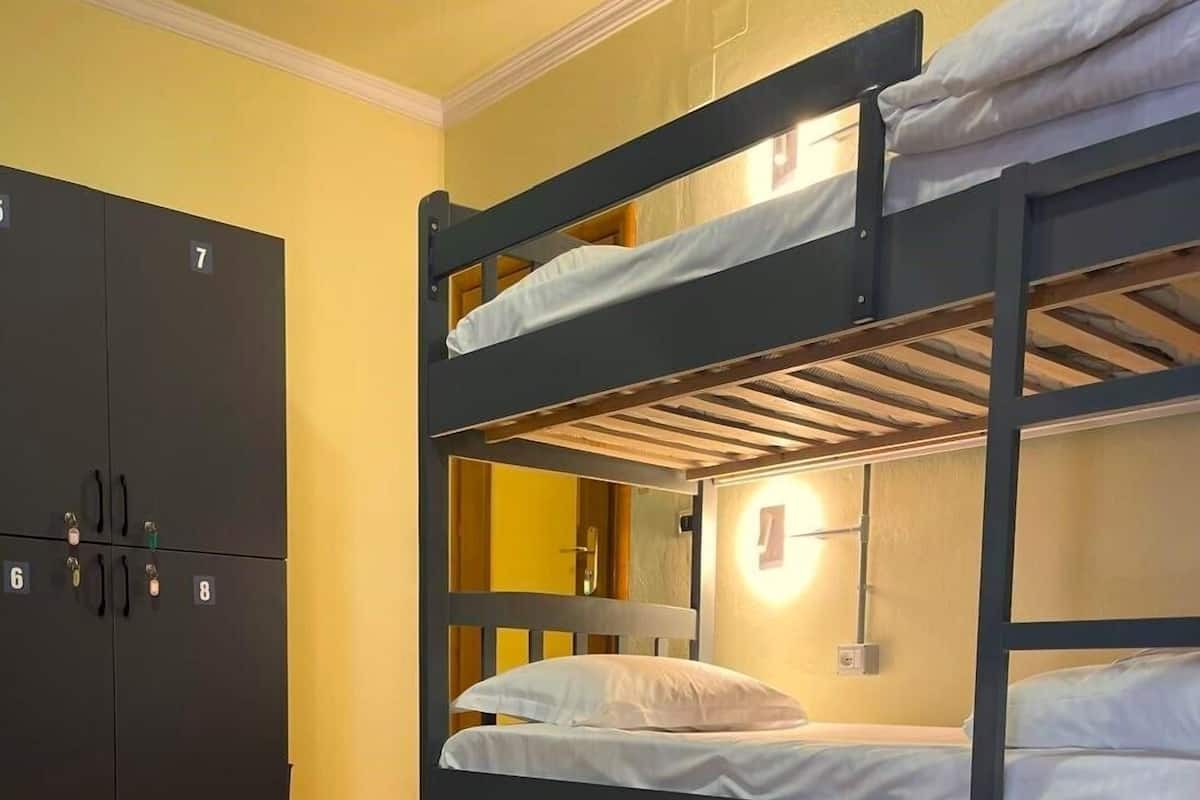 A bunk bed room with a wooden floor, a wardrobe with numbered compartments, and a wall-mounted light fixture.