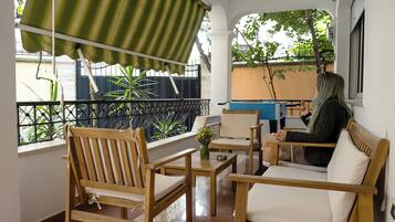 A balcony with wooden furniture, a green striped awning, and a view of the outside.