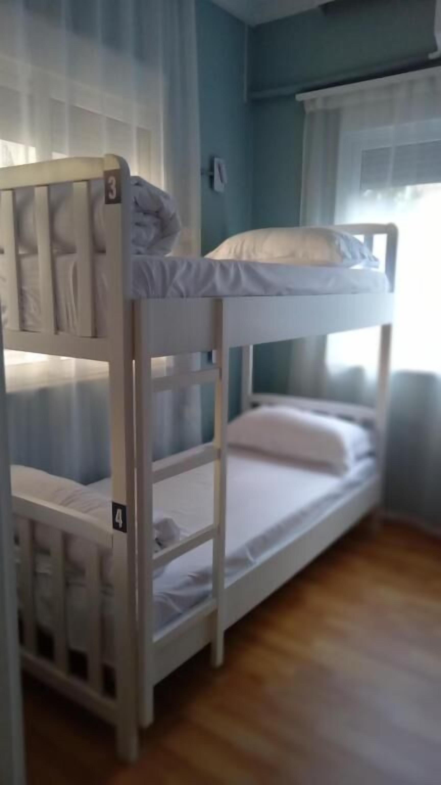 A bunk bed with two levels, a window with curtains, and a wooden floor.
