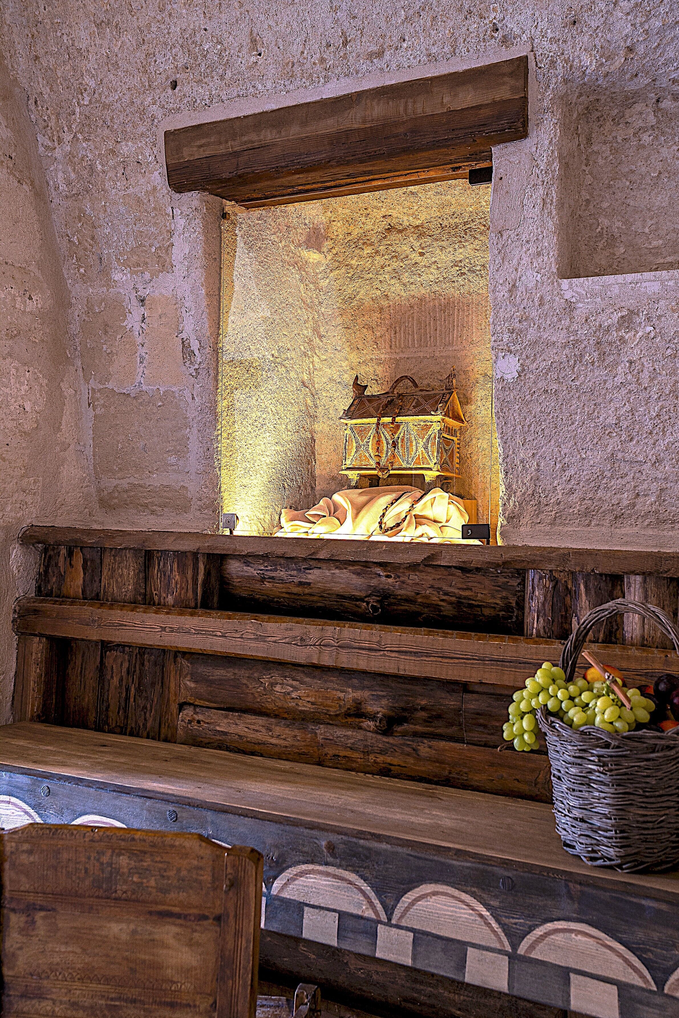 A rustic stone wall with a wooden bench and a wicker basket of grapes.