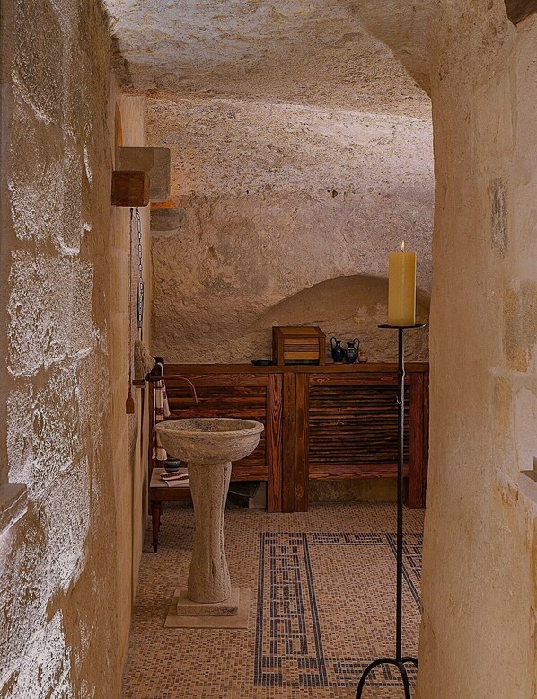 Un intérieur rustique avec un mur en pierre, un banc en bois, un lavabo en pierre et une bougie posée sur un chandelier.