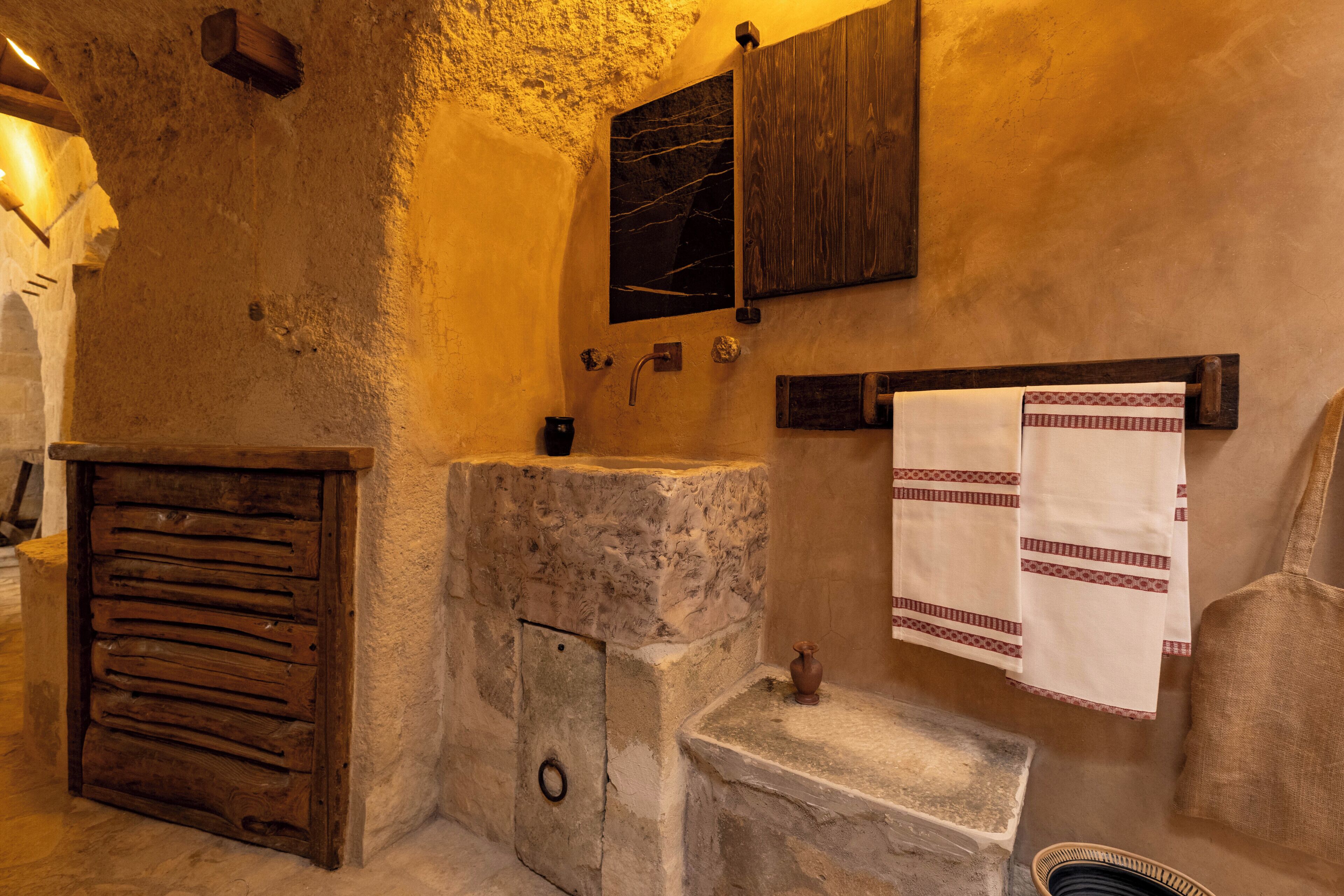 A rustic bathroom with a stone sink, wooden cabinets, and a towel rack.