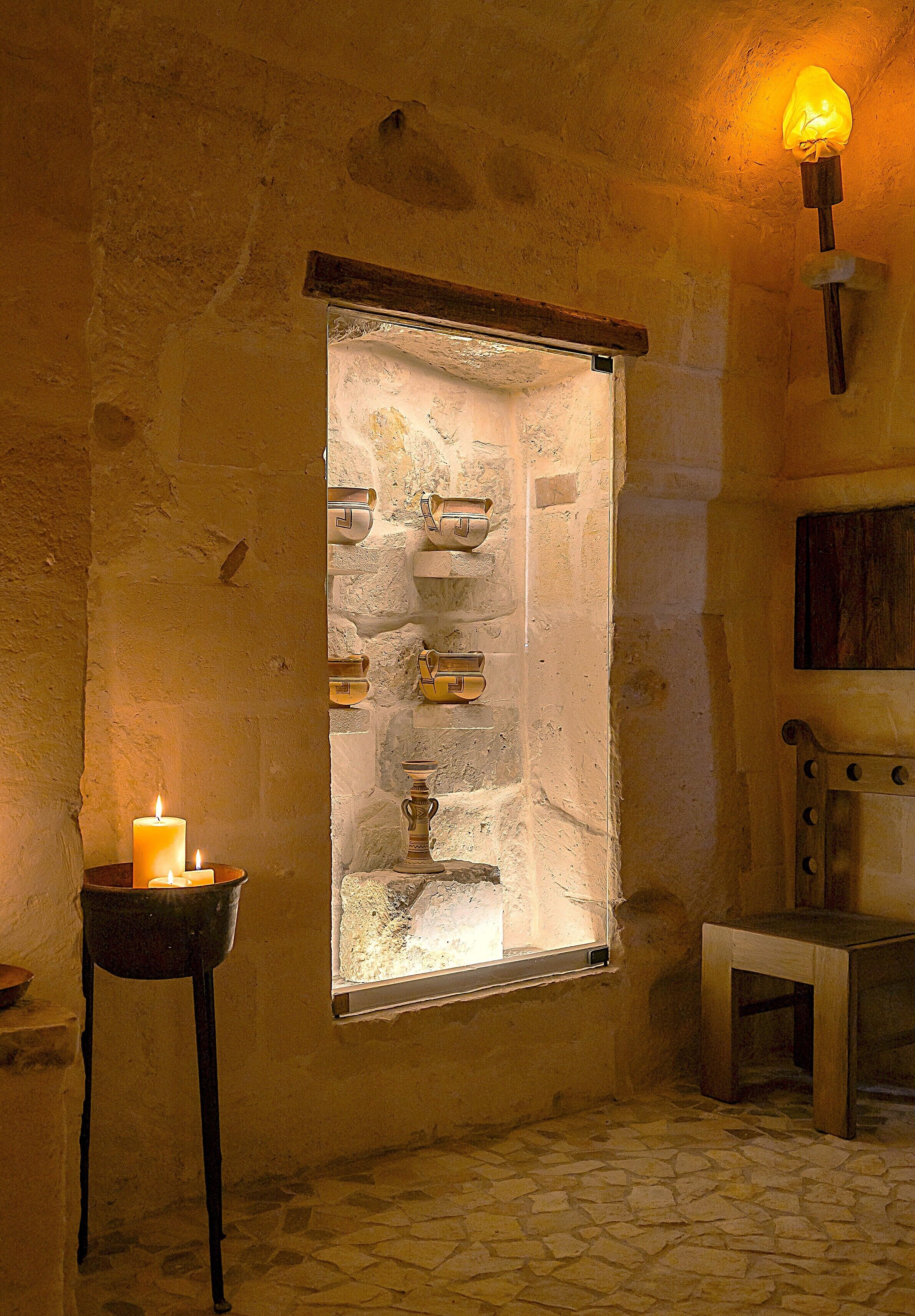 A stone wall with a window, a candle, and a wooden table.