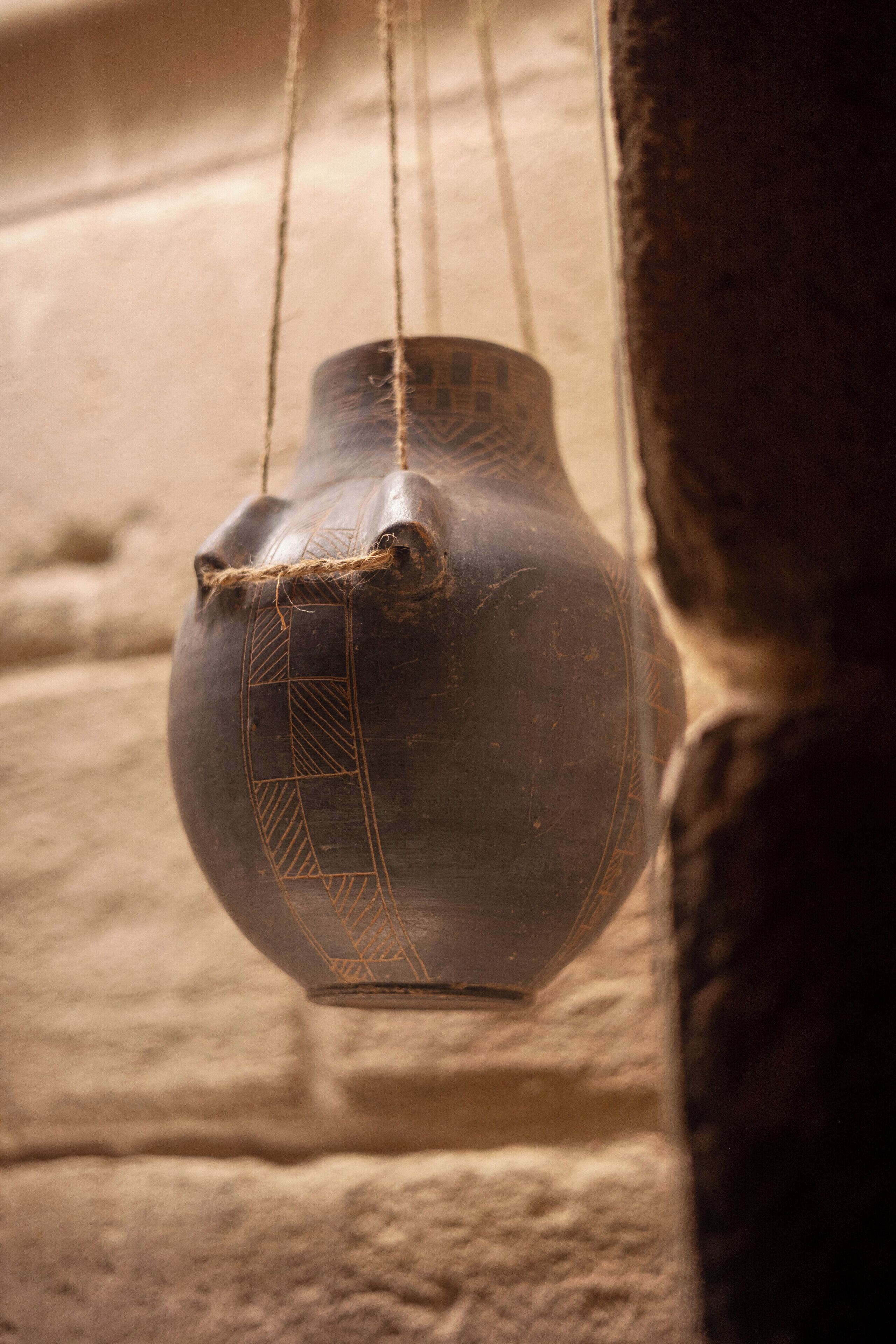A hanging pottery piece with geometric patterns, suspended by strings.