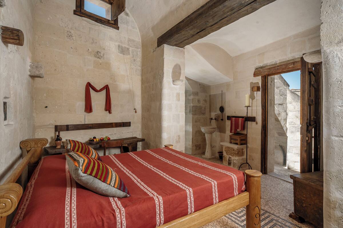 A traditional room with a wooden bed, stone walls, and a stone fireplace.