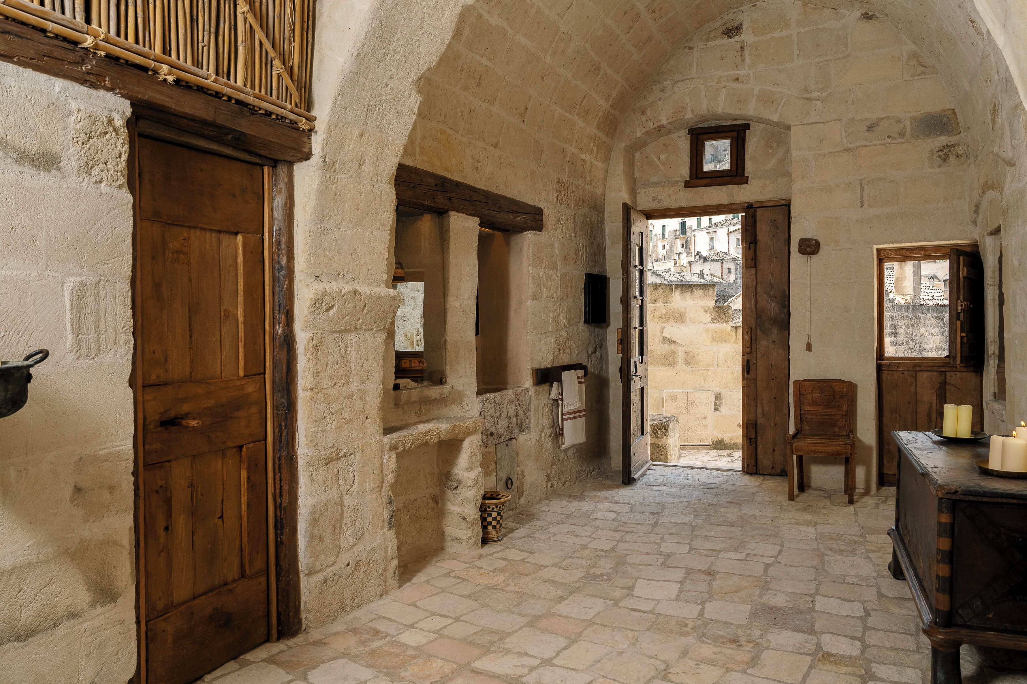 An arched stone hallway with a wooden door, a small window, and a chair.