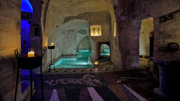 Un interior con pared de piedra, una pequeña piscina y suelo de baldosas.