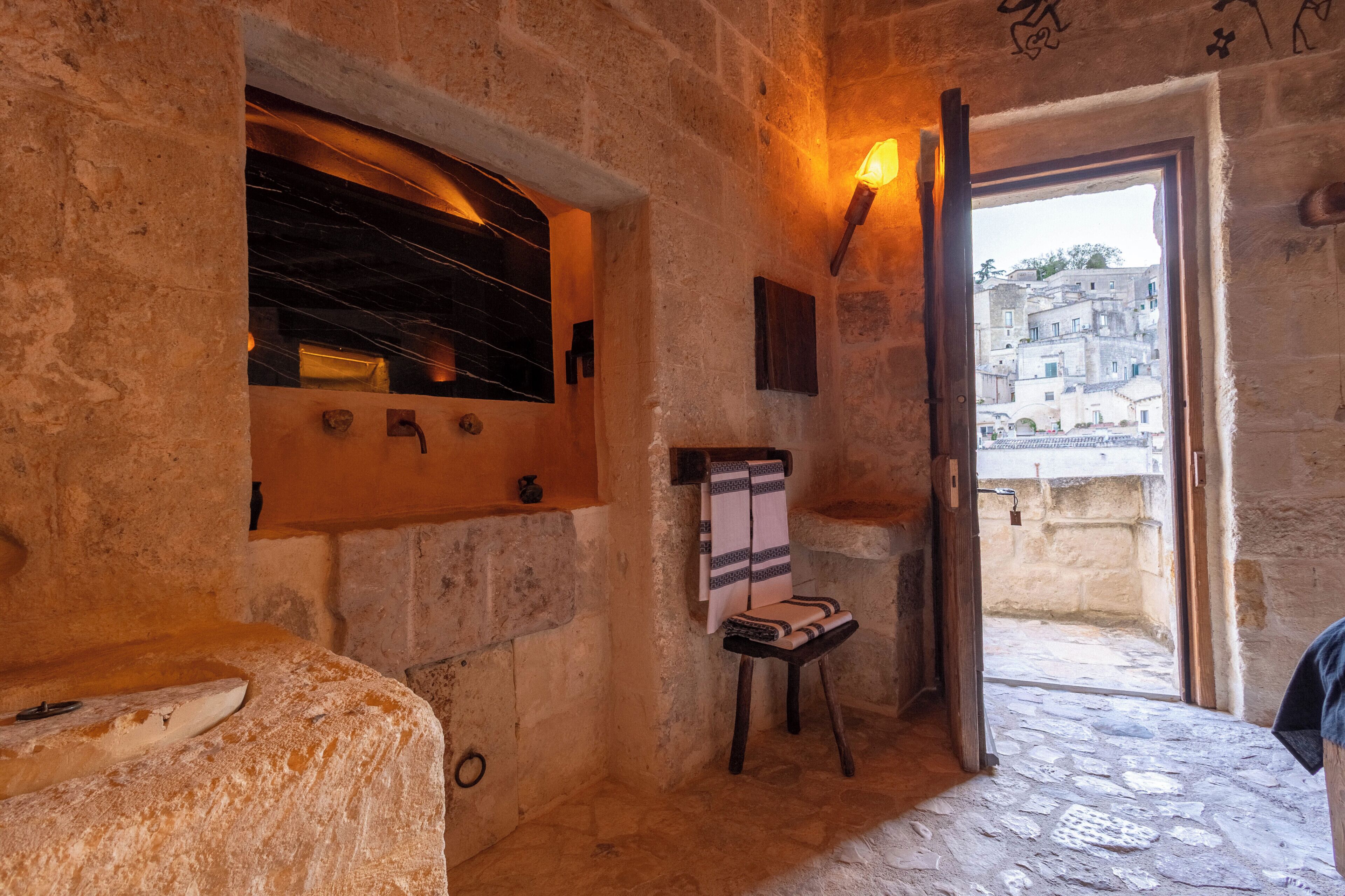 A stone-walled room with a window, a towel rack, and a chair.