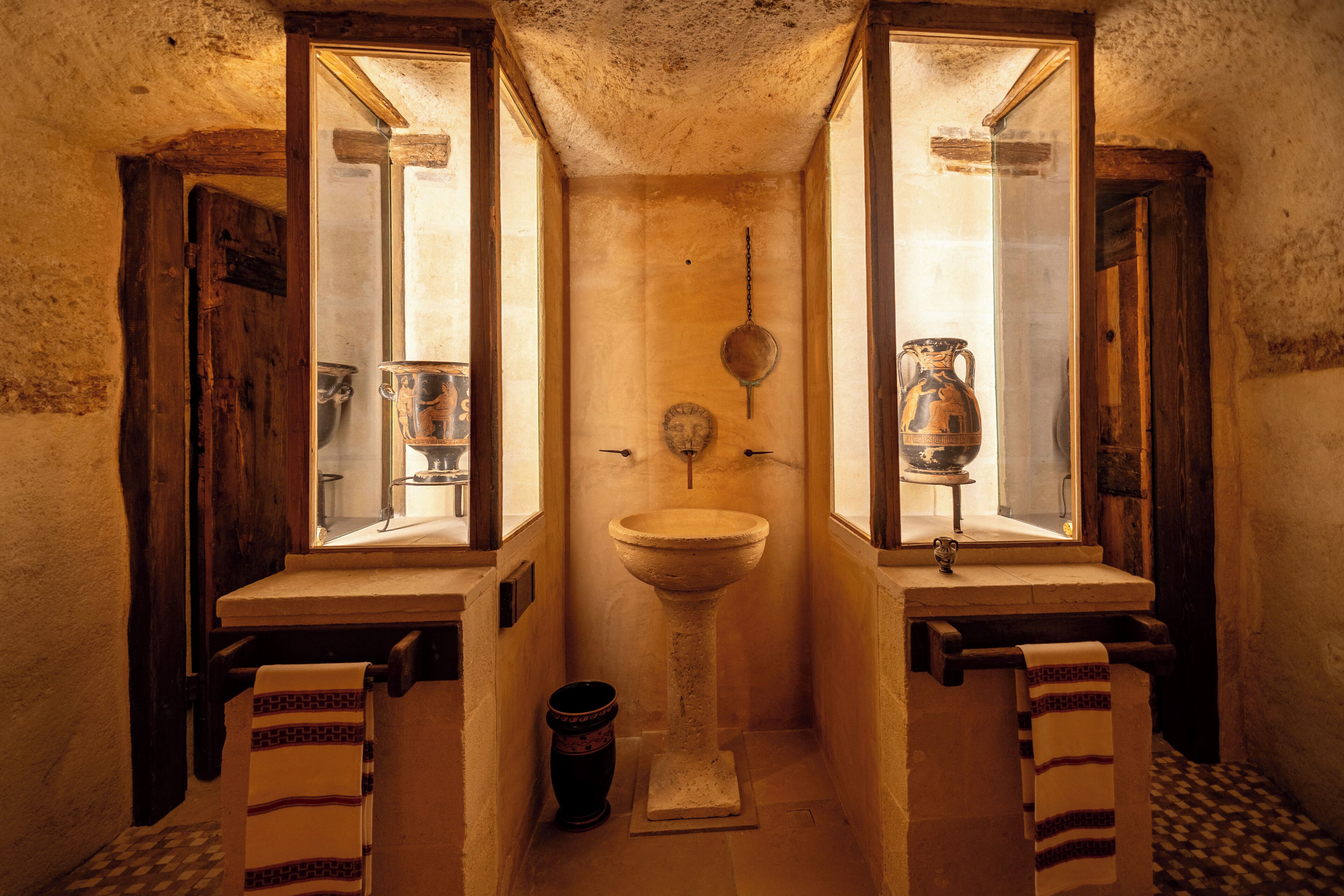 A narrow bathroom with a central sink, two windows, and a hanging light fixture.