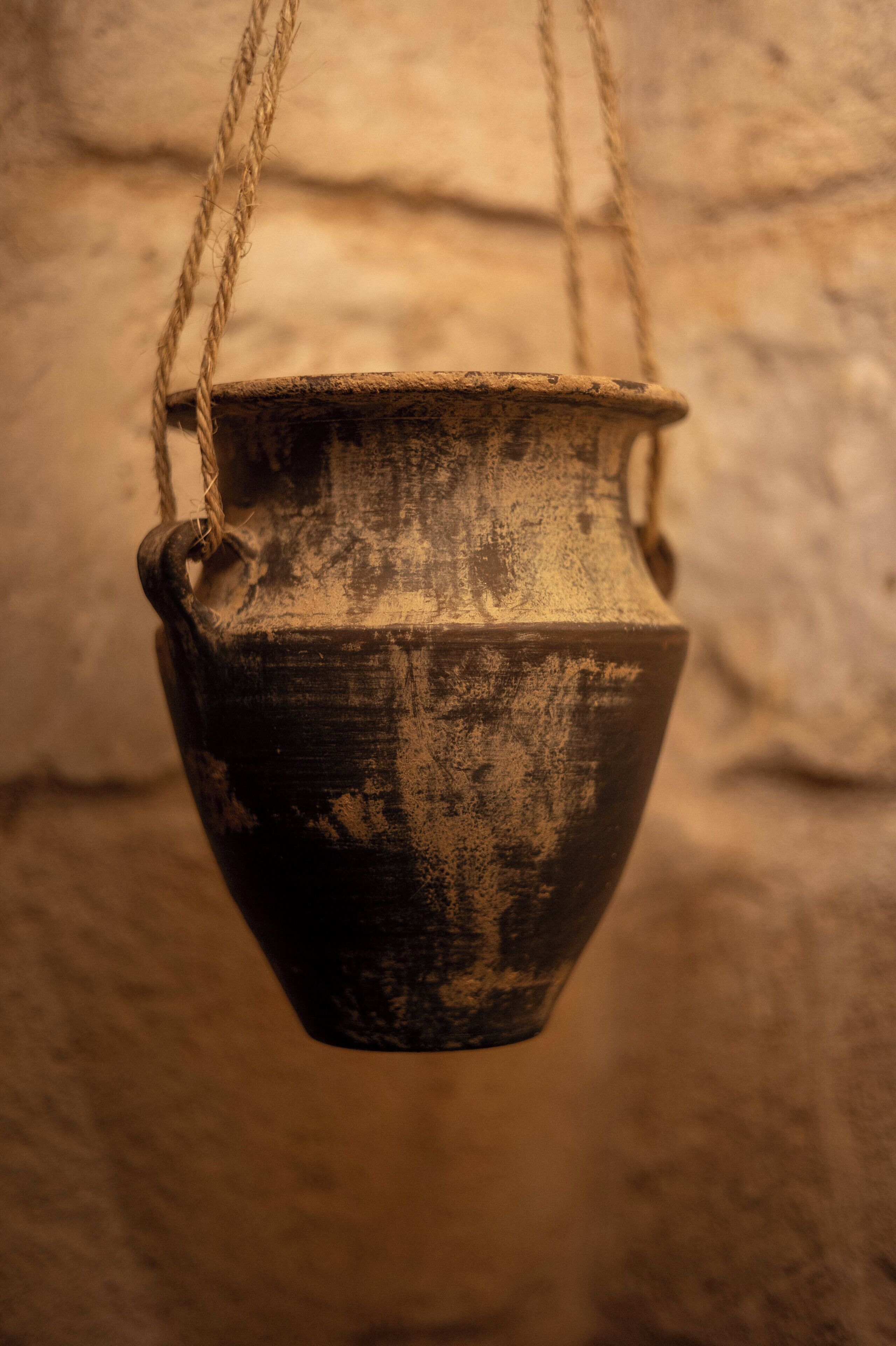 Una olla colgante con cuerda, frente a una pared texturizada.