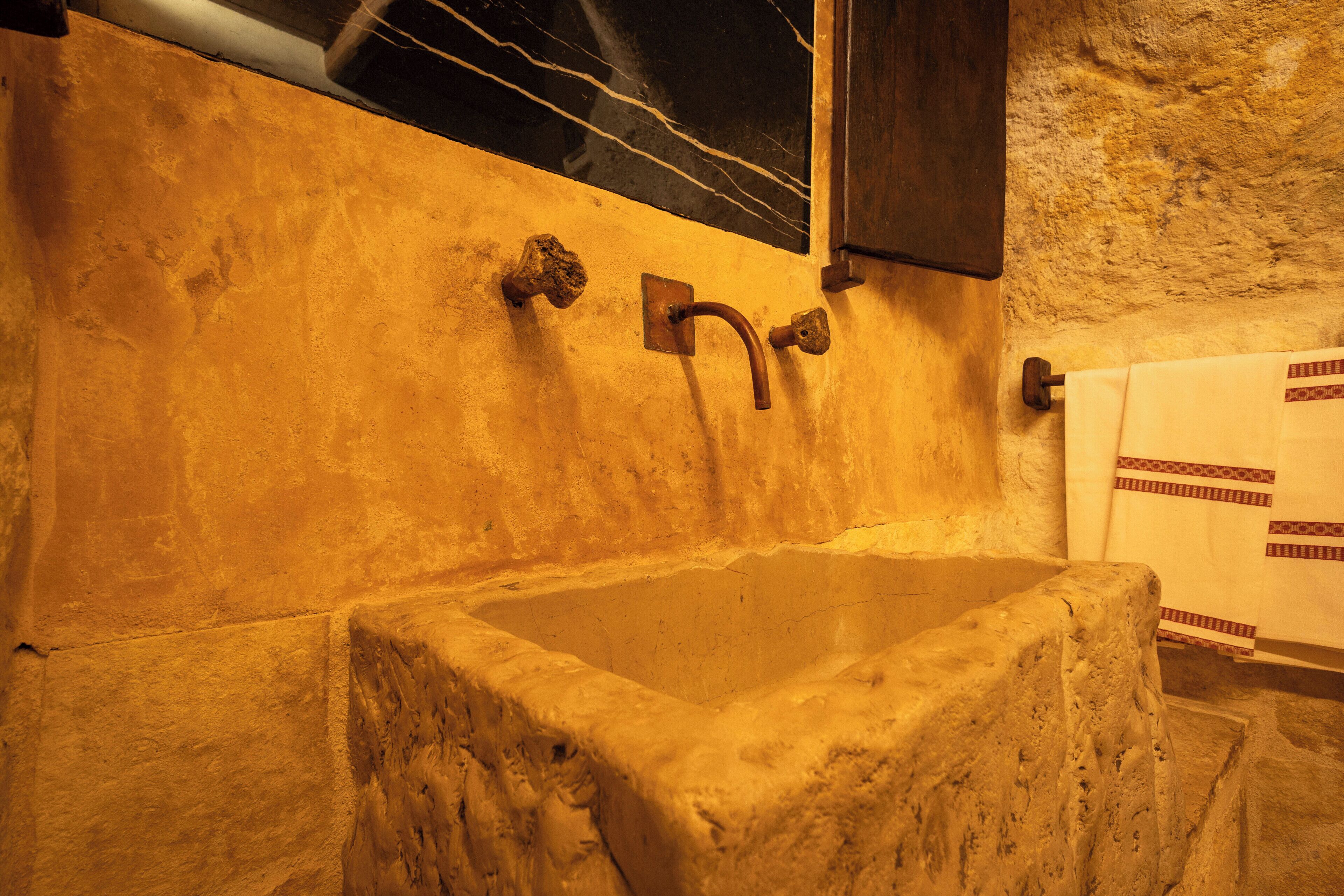 A stone sink with a faucet, a marble backsplash, and a towel rack with patterned towels.