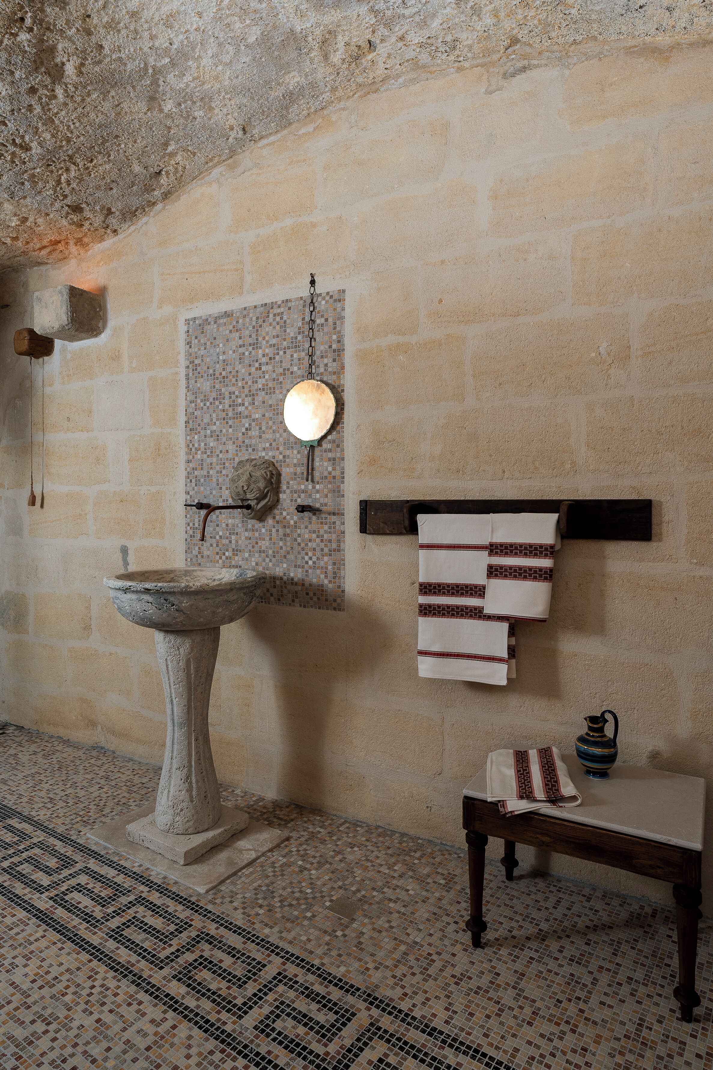 Ein Badezimmer mit einem Steintonne, Mosaikfliesen, einer Holzwand mit Handtüchern und einem kleinen Tisch mit einer Vase.