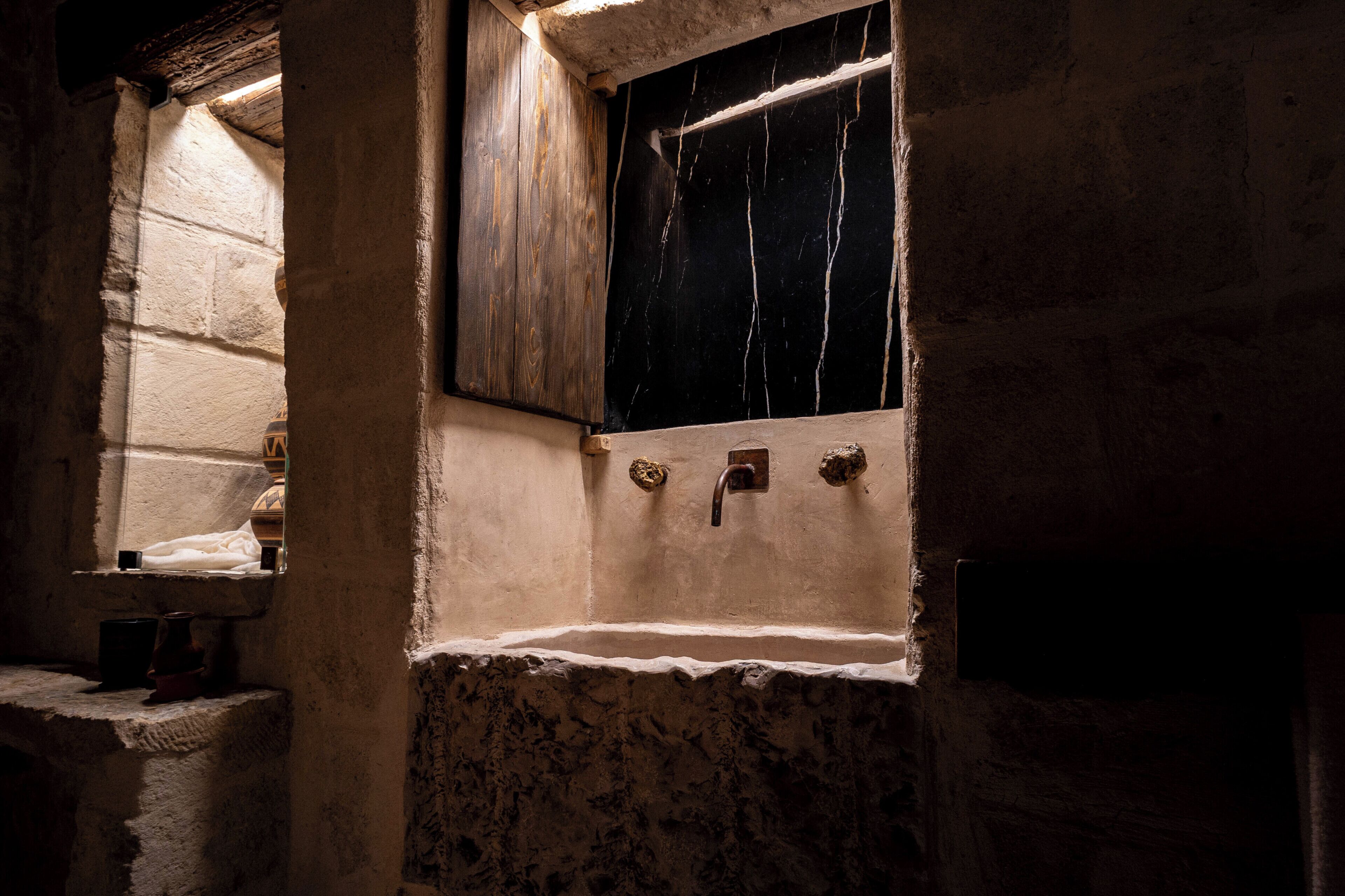 A stone-walled bathroom with a wooden window, a sink, and a mirror.