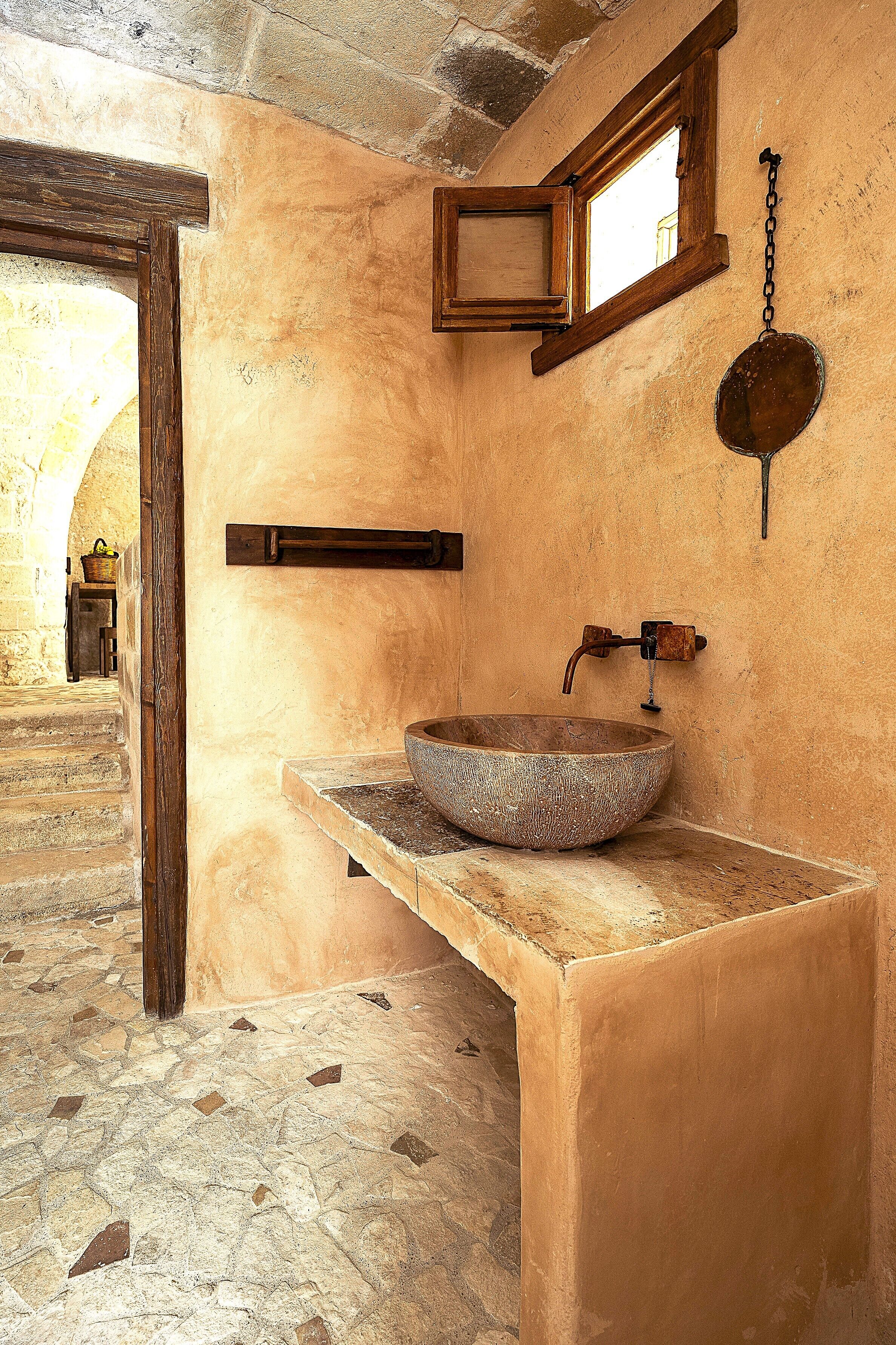 Un baño rústico con un lavabo de piedra, un banco de madera y una ventana pequeña.