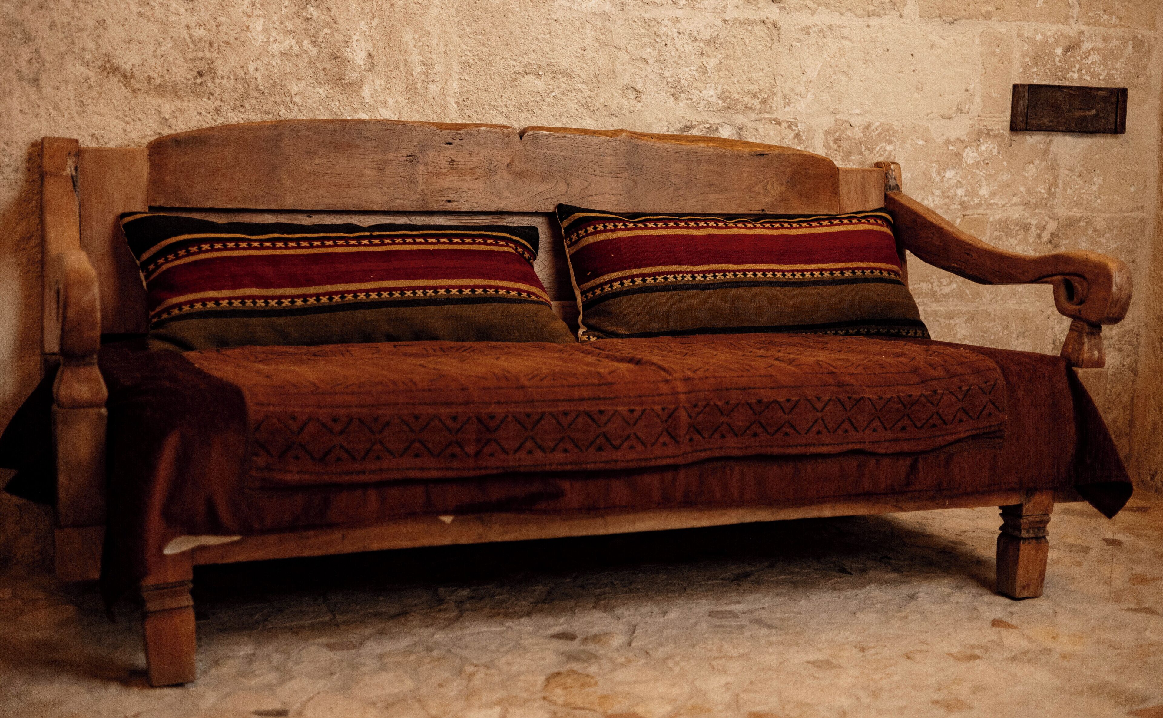 A wooden sofa with patterned cushions against a textured wall.