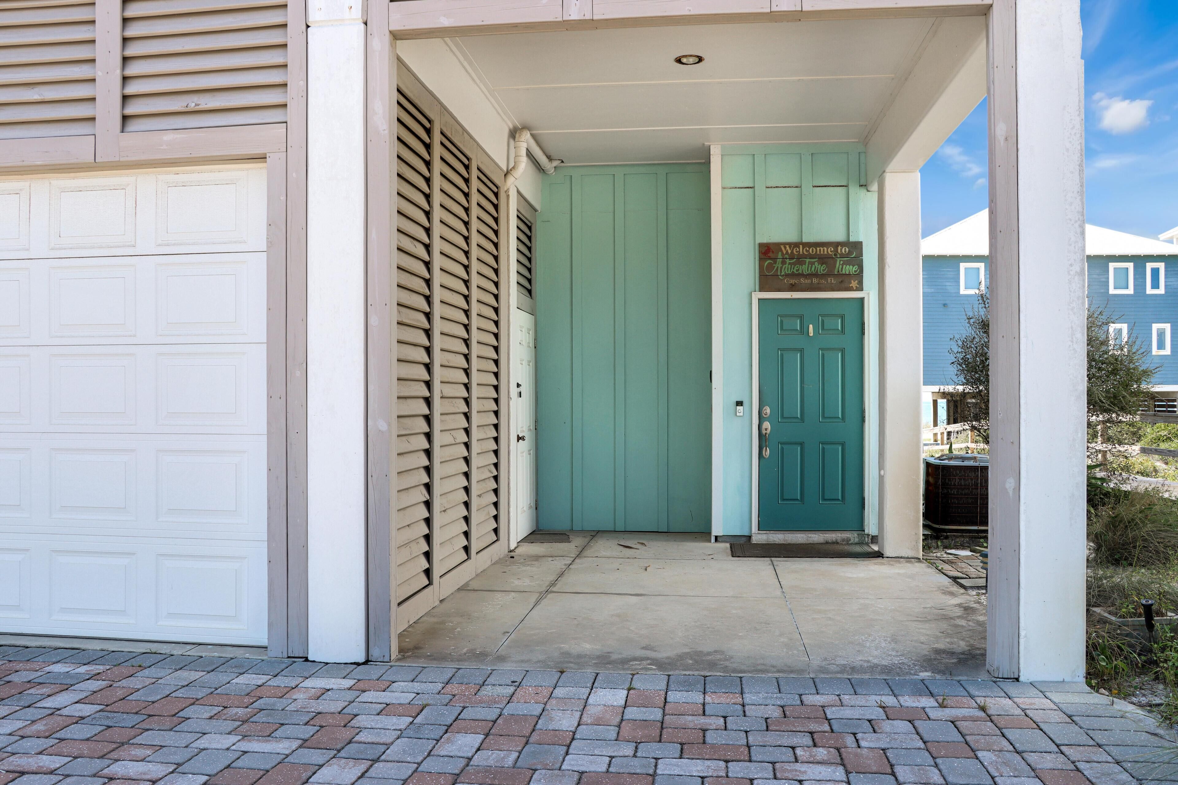 A house entrance with a teal door, a garage door, and a brick pathway.