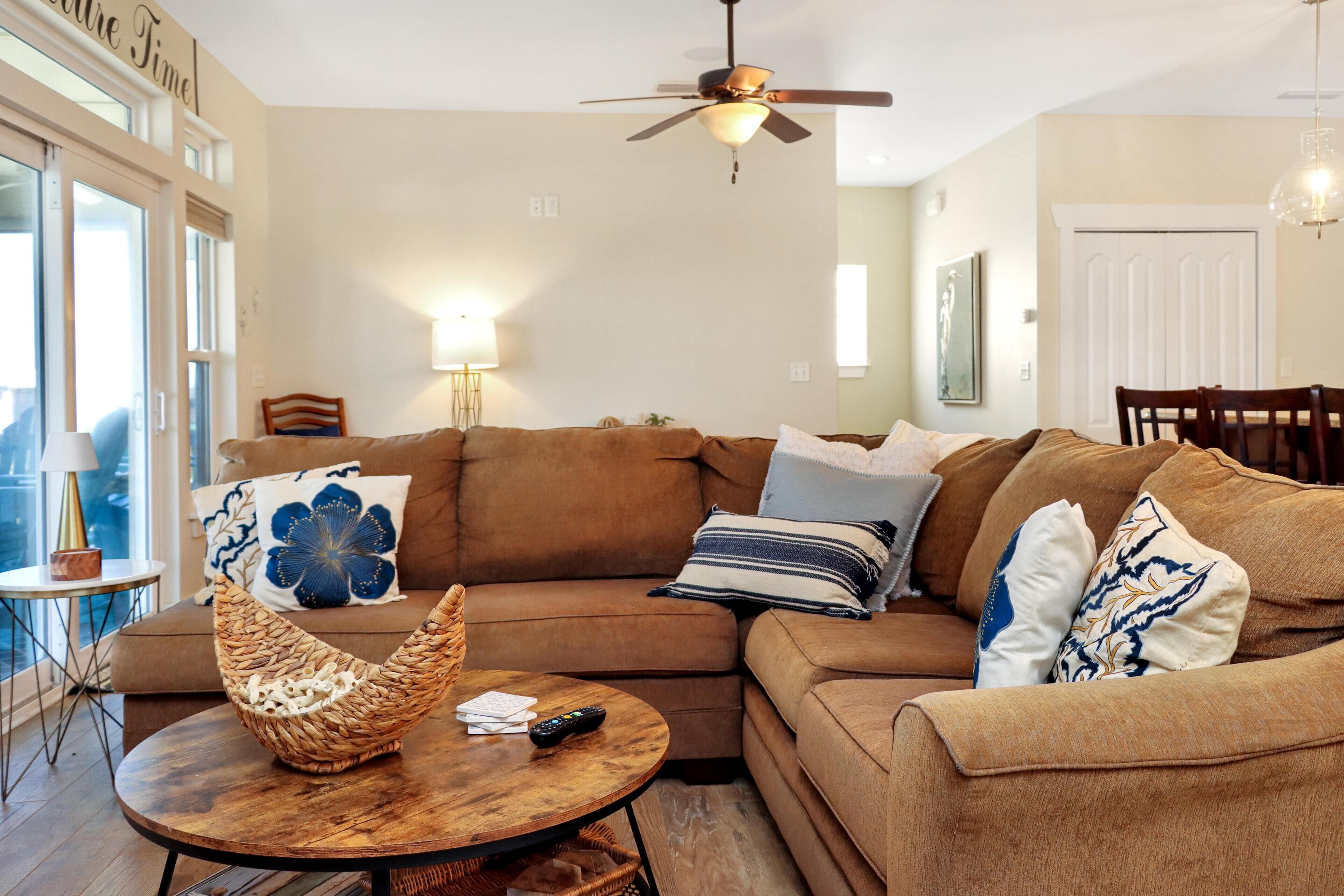 A cozy living room with a sectional sofa, a round wooden coffee table, and a ceiling fan.