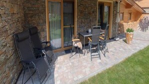 A covered patio with stone walls, a table with chairs, and a black lounge chair. - Apartment in Leutasch Near Ski Trails (Leutasch)