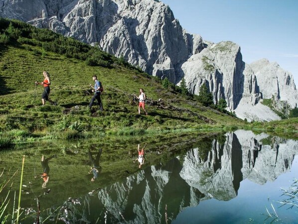 A group of people hiking on a grassy slope with a lake reflecting the surrounding mountains. - Apartment in Leutasch Near Ski Trails (Leutasch)