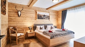 A wooden cabin bedroom with a bed, a chair, a nightstand, and a mounted deer skull. - Apartment in Leutasch Near Ski Trails (Leutasch)