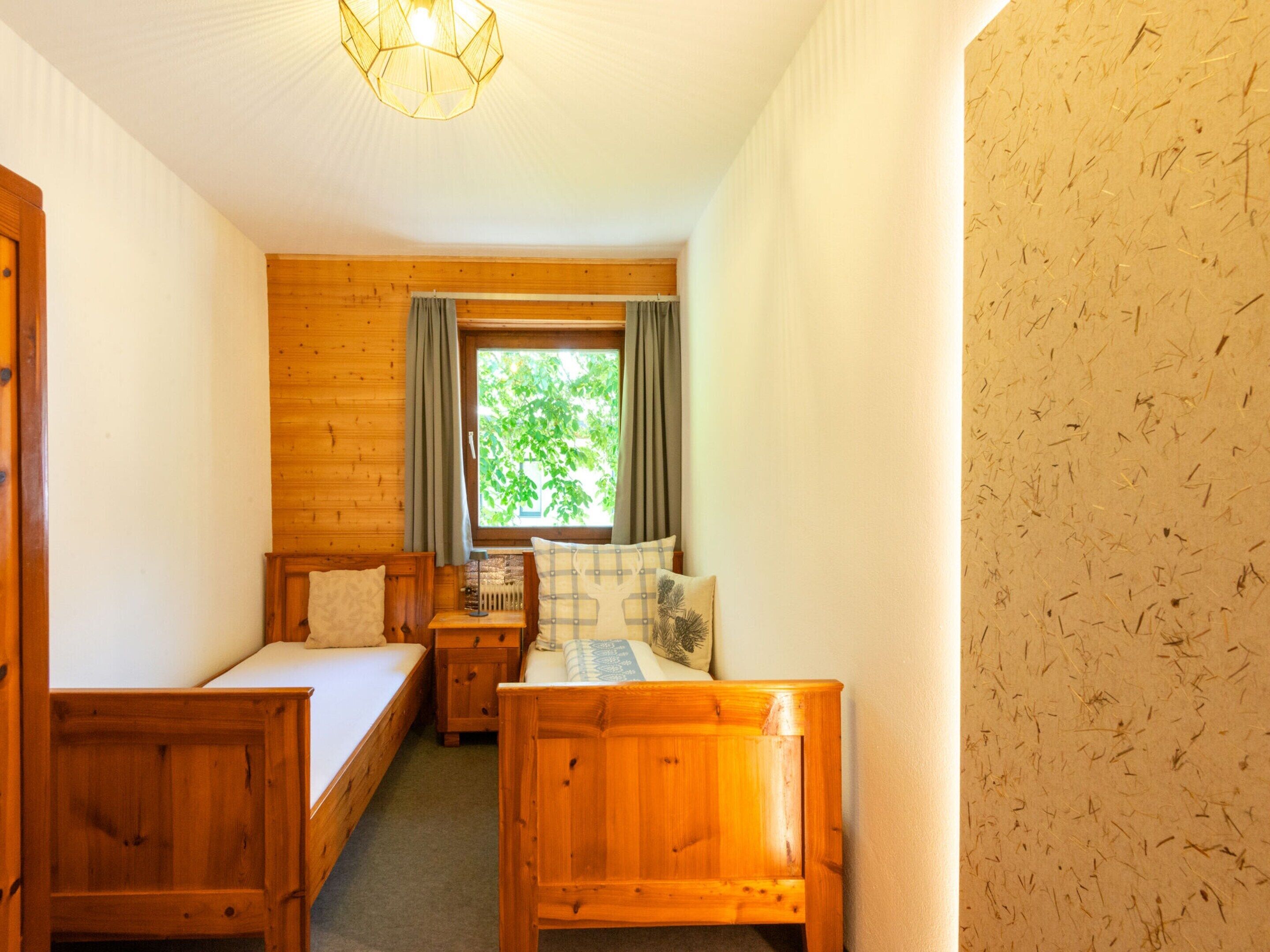 Een kamer met twee houten bedden, een tafeltje en een raam met gordijnen.