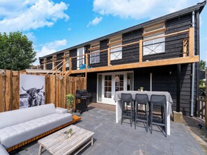 Un edificio a due piani con un patio che include un divano, un tavolo con sedie e un barbecue.