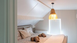 A bedroom with a sloped ceiling, a bed with patterned bedding, a hanging light fixture, and a radiator. - Cozy Villa w/ Sauna and BBQ (Hattemerbroek)