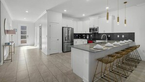 Una cocina moderna con armarios blancos, electrodomésticos de acero inoxidable y una isla central con taburetes de bar.