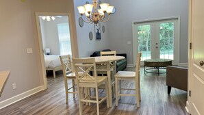 A dining area with a wooden table and chairs, a chandelier, and a view of a bedroom with a bed and a window.