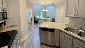 A modern kitchen with a dishwasher, stainless steel sink, and a dining area with a chandelier.